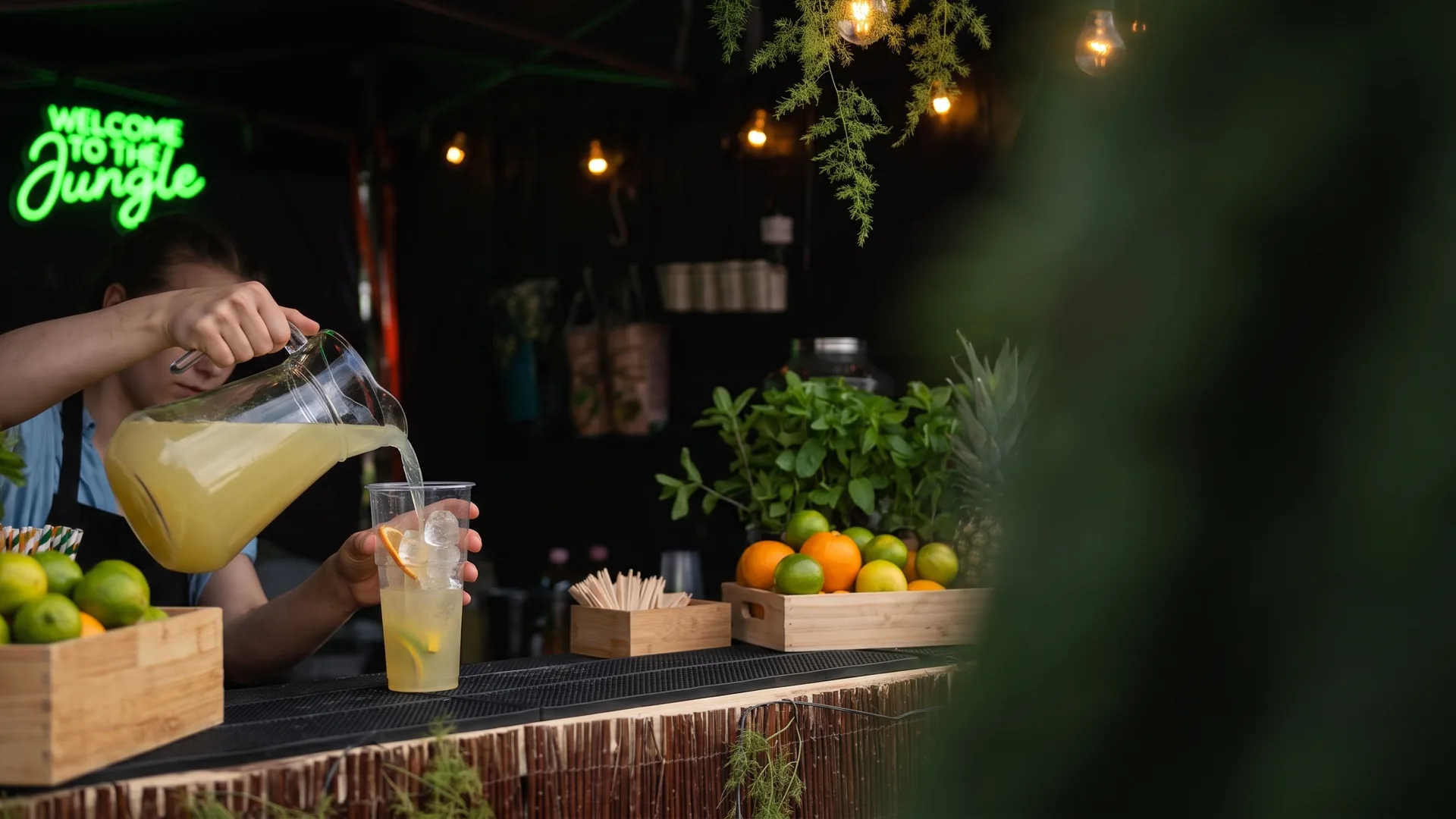 Barmanka nalewa lemoniadę z dzbanka do kubka na bambusowej ladzie stoiska Forest