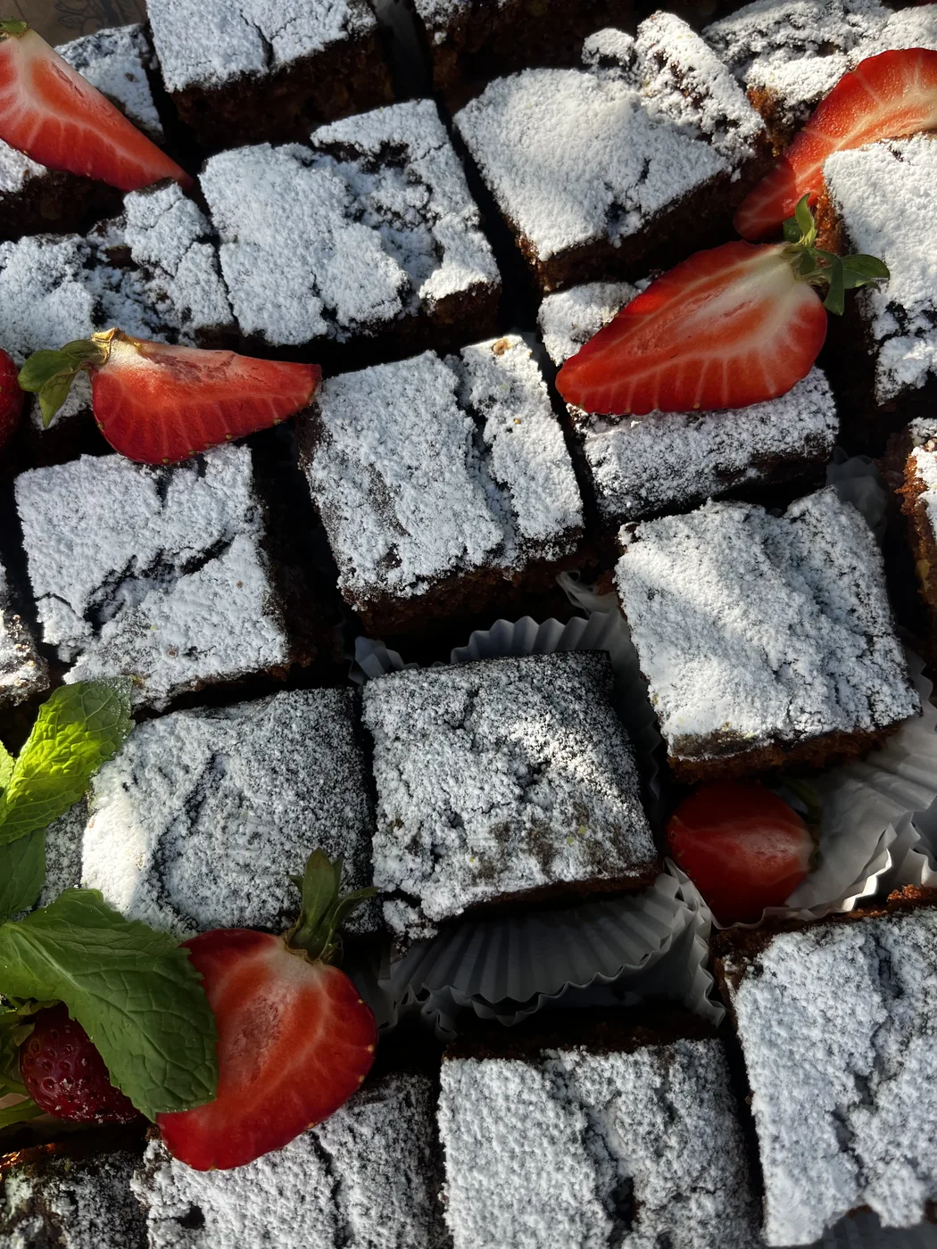 Kawałki brownie z cukrem pudrem, truskawkami i miętą