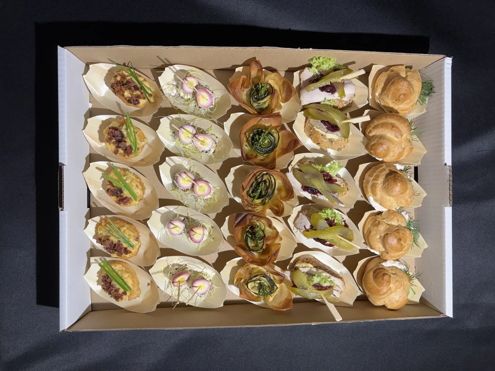 Pudełko finger food z góry: tartaletki, ptysie, roladki w papierowych łódeczkach