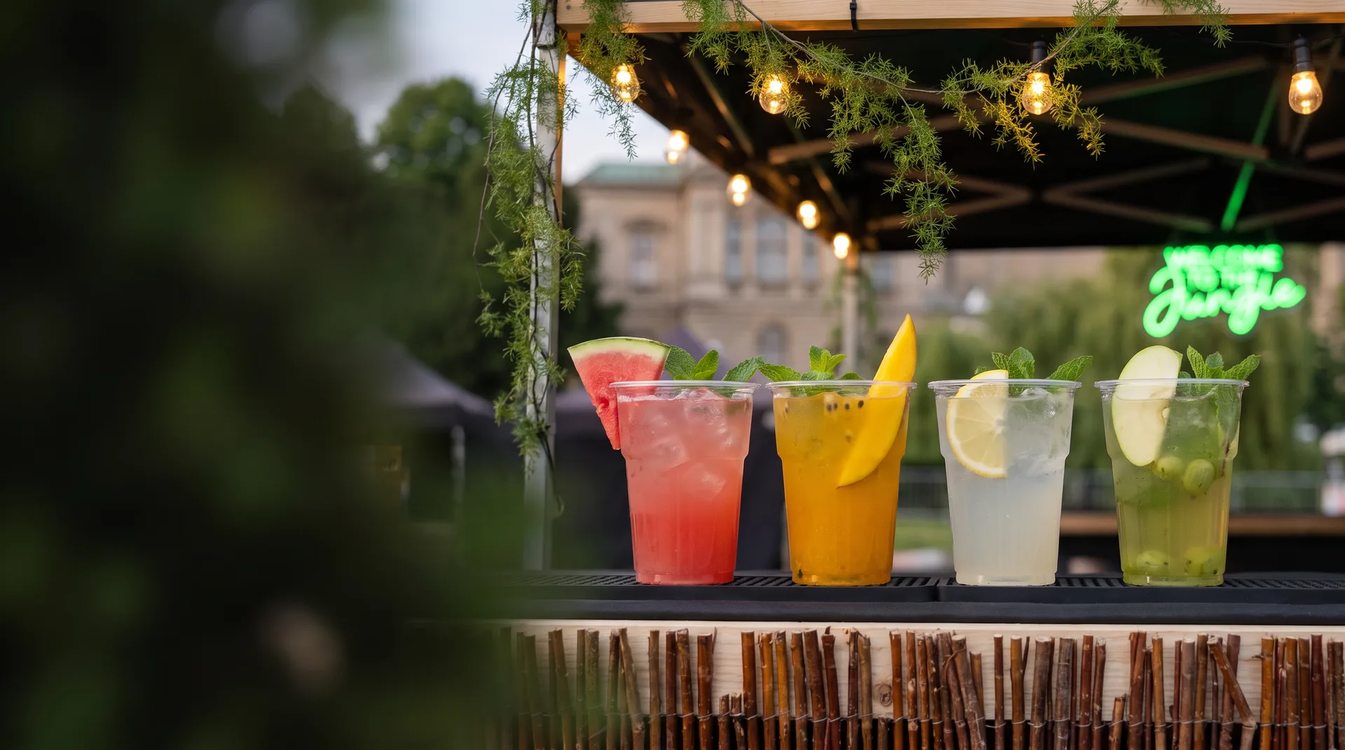 Cztery lemoniady w kubkach na ladzie stoiska: arbuzowa, mango z marakują, cytrynowa i ogórkowa z miętą